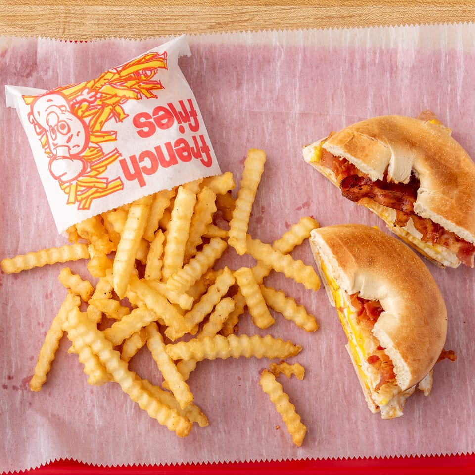 Crinkle-cut french fries spilling from a bag next to two bacon, egg, and cheese bagels.