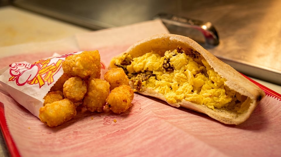 A pita bread sandwich filled with scrambled eggs and a side of crispy tater tots.